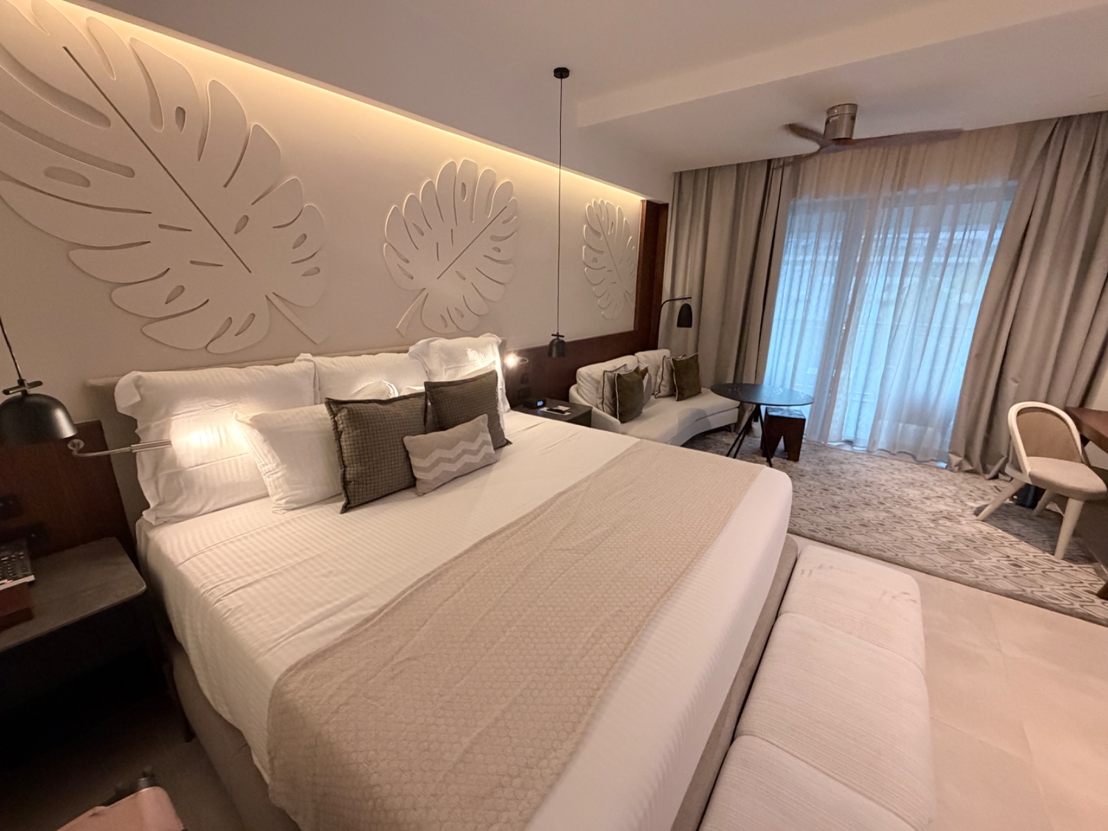 A king suite at Secrets Playa Esmeralda with a palm-leaf feature wall, sitting area, and doors out to the balcony. Photo: Dreams Fulfilled Travel Dream Designer